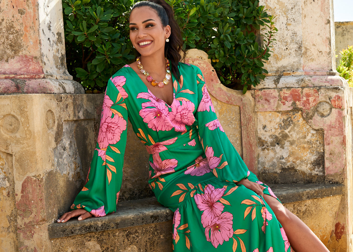 Models wearing a green and pink floral long sleeve dress with multi colored crystal necklace.